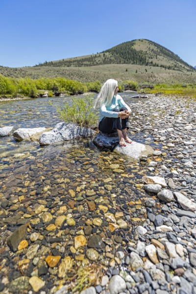 USA, Idaho, Sun Valley, Woman sitting on rock in river