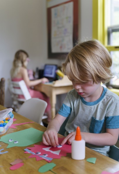 Boy (4-5) preparing paper cutout, girl (6-7) in background