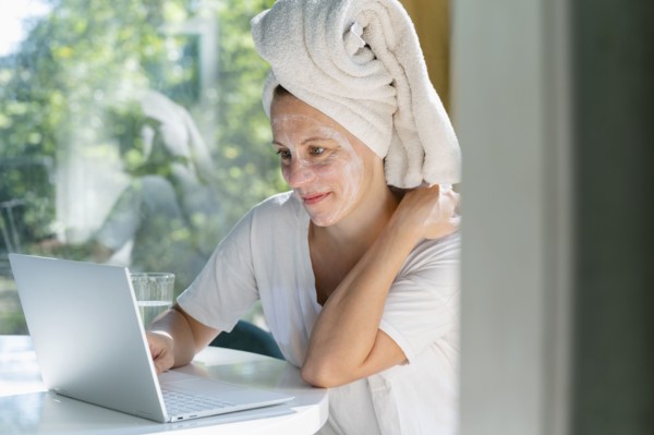 Woman with face mask and towel on head using laptop at table