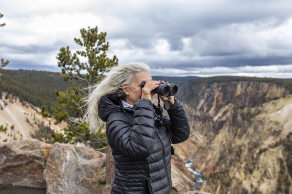 Senior woman looking through binoculars while standing above Grand Canyon in Yellowstone National Park