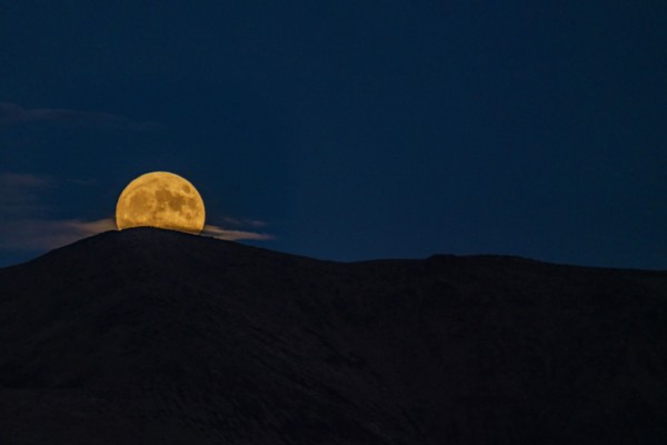 Full moon rising over mountains at night