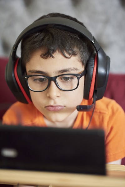 Boy (8-9) gaming on tablet while sitting in bed during weekend