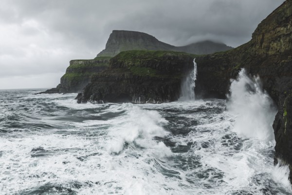 Coastline with Mulafossur Waterfall falling into Atlantic Ocean in stormy day
