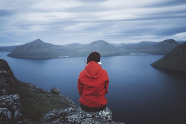 Woman sitting on edge of cliff over sea and looking at view