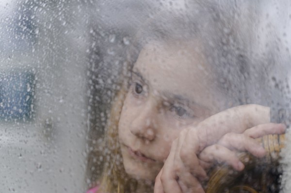 Close-up of girl (8-9) looking through window on rainy day