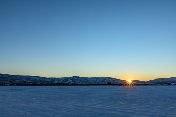 Sun setting over snowy field and mountains