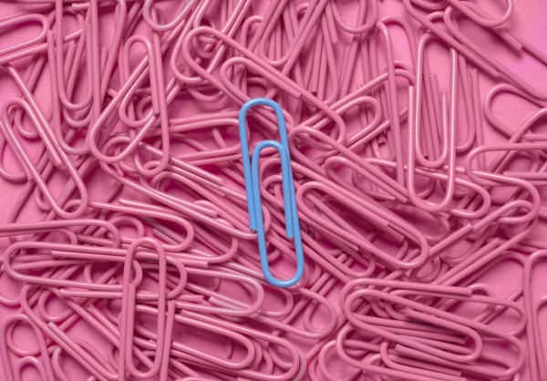Blue paper clip on pile of pink paper clips