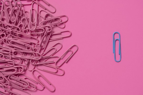 One blue paper clip and pile of pink paper clips