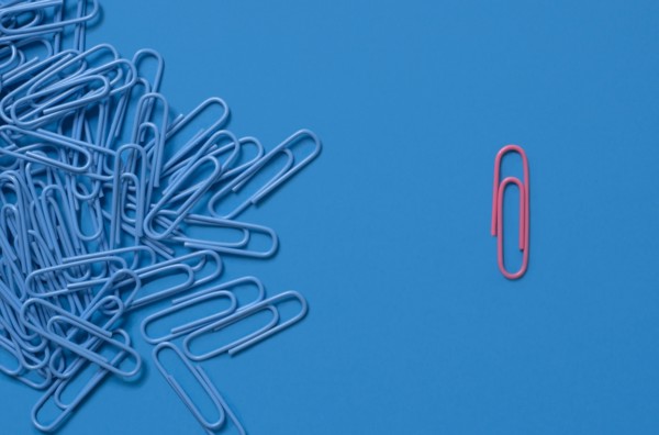One pink paper clip and pile of blue paper clips