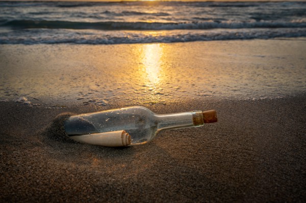 Glass bottle with message inside on beach at sunset