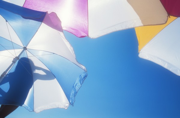 Low angle view of silhouette of woman on beach umbrella against blue sky