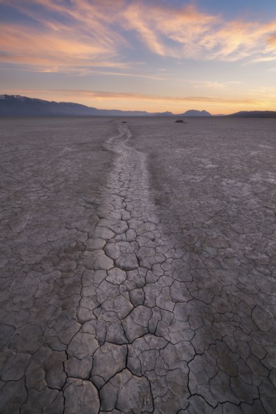 Path at cracked desert area at sunset
