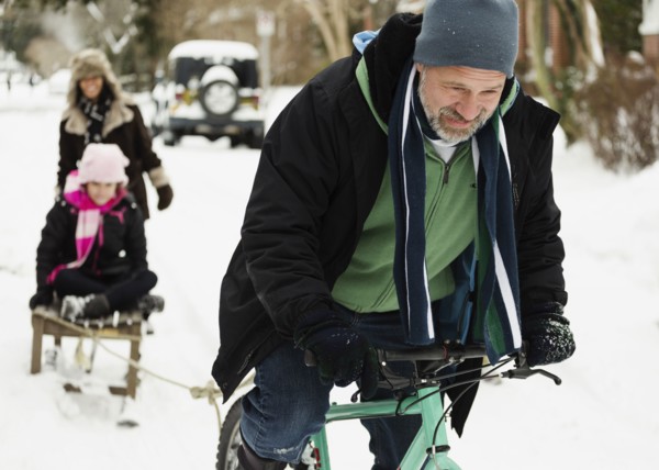 Parents and daughter playing with toboggan in snow