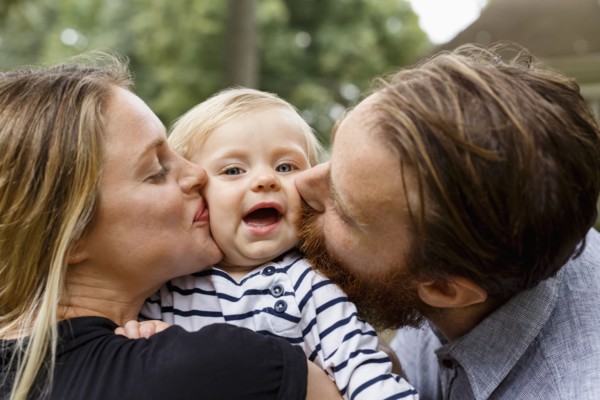 Mother and father kissing baby girl on cheek