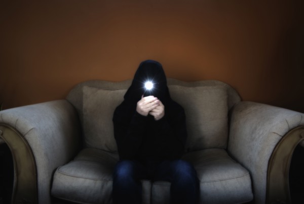 Man in hood sitting on sofa and holding flashlight in front of his face