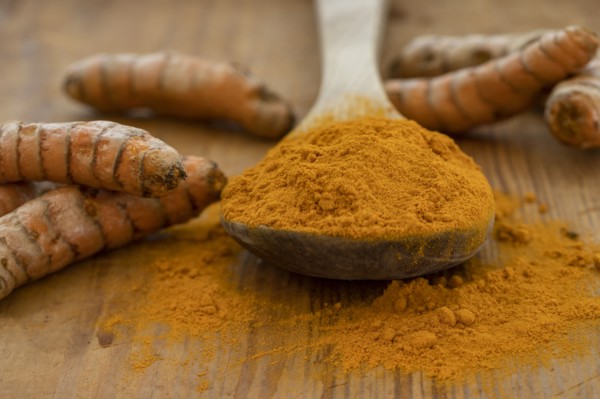 Turmeric powder and root on wooden surface