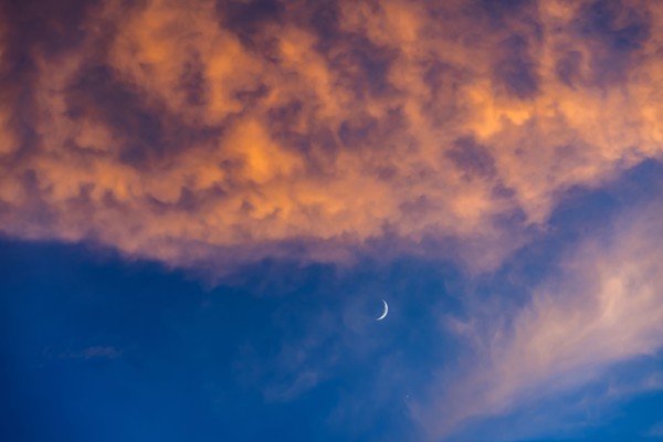 Crescent moon against blue sky with pink and orange clouds