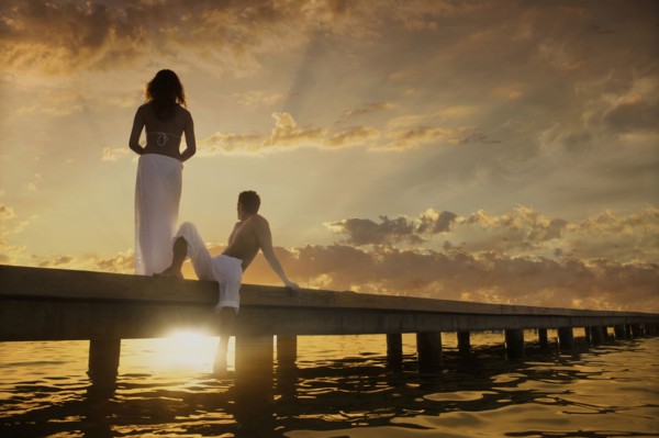 Caucasian couple admiring sunset from dock over ocean