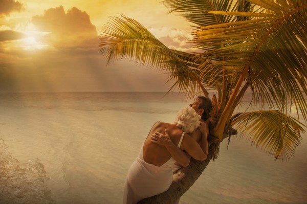 Older Caucasian couple hugging on palm tree at beach