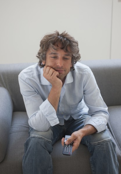 Bored Caucasian man sitting on sofa watching television