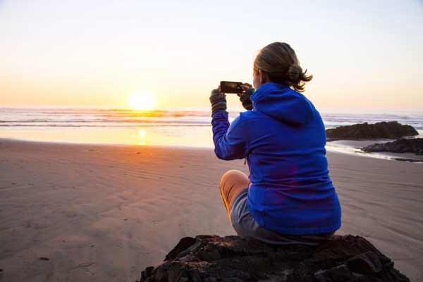 Caucasian woman taking picture of sunrise on beach