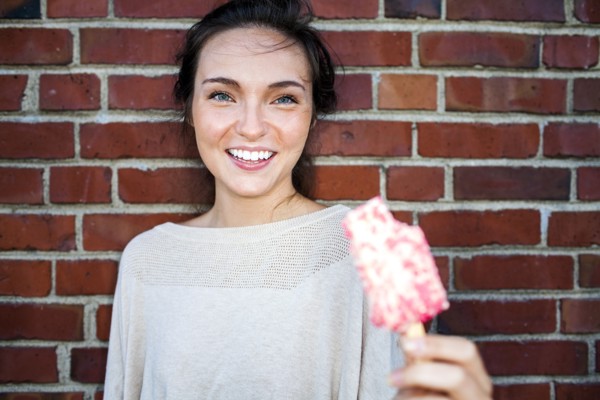 Caucasian woman eating ice cream near red brick wall