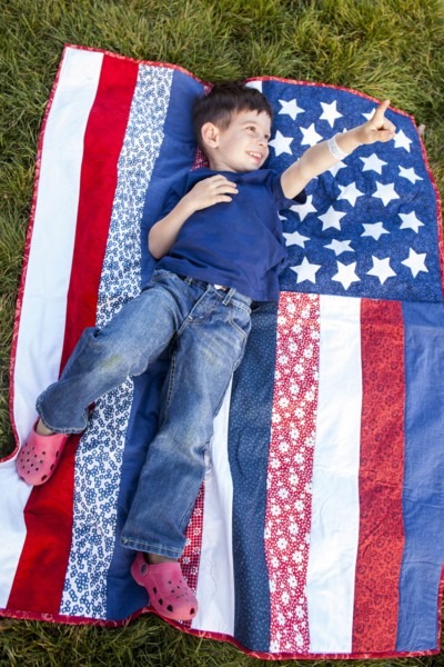 Mixed race boy pointing up on American flag blanket on grass