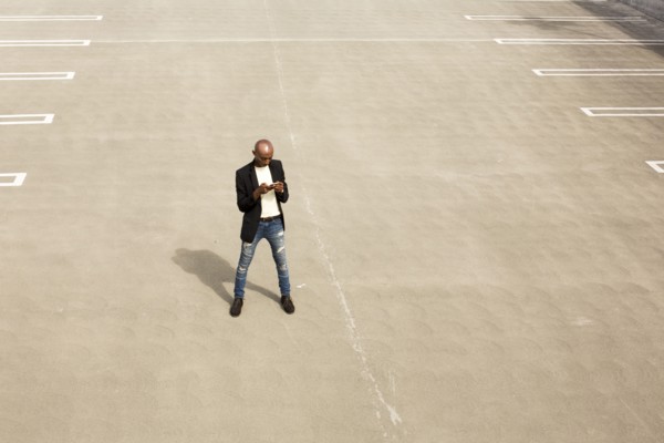 Gay Black man texting in empty parking lot