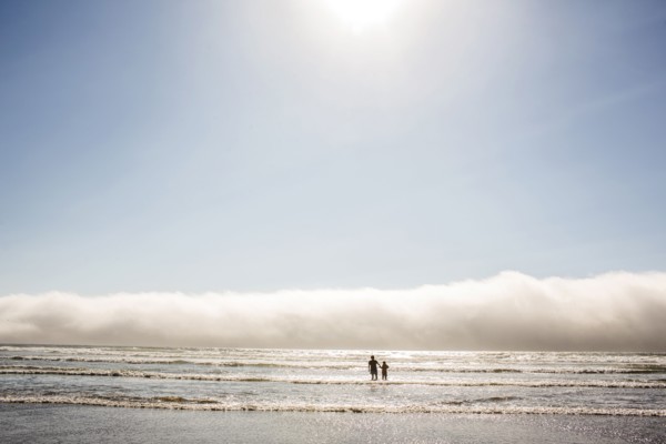 Caucasian mother and son wading in ocean waves at beach