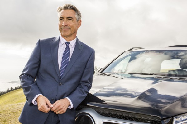 Smiling Caucasian businessman leaning on car