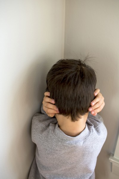 Mixed Race boy standing in corner covering ears