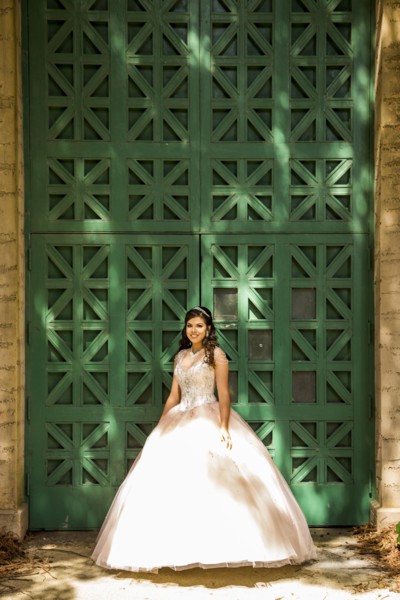 Smiling Hispanic girl wearing gown near green wall