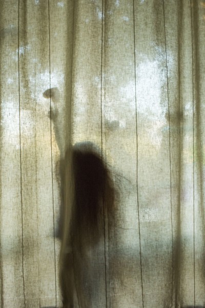 Silhouette of Caucasian girl touching heart-shape behind window curtain