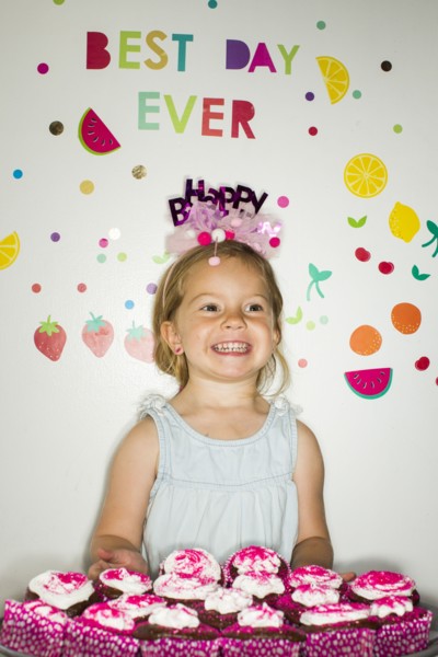Caucasian girl holding tray of cupcakes for birthday