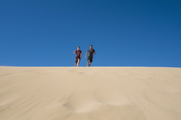 Caucasian father and son running on sand dune