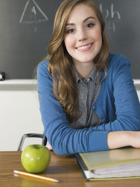 Student with apple smiling at desk in classroom