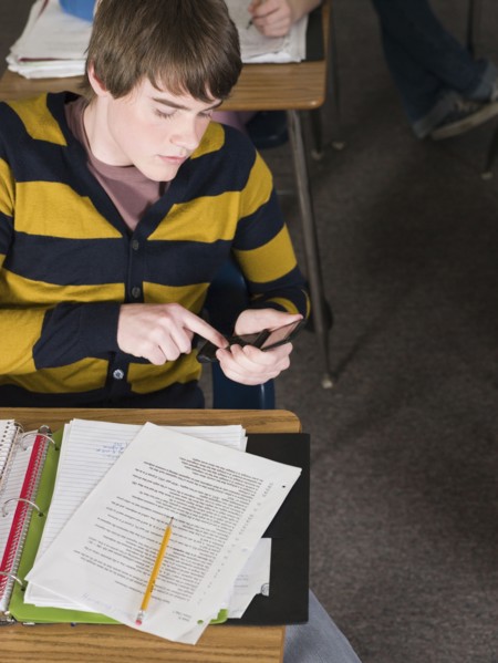 Student using cell phone at desk in classroom