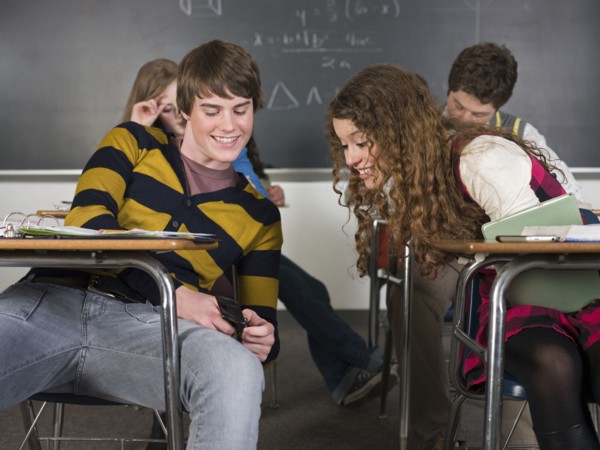 Students using cell phone at desk in classroom