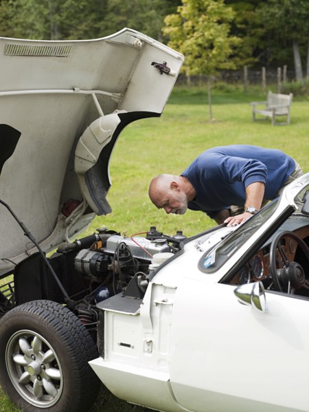 Older man examining broken-down convertible in park