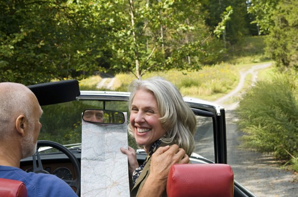 Older couple driving convertible on dirt road