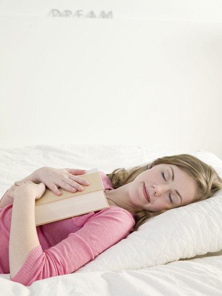 Caucasian woman napping with book on bed