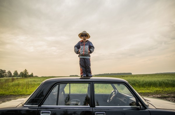 Caucasian boy standing on car roof in rural field