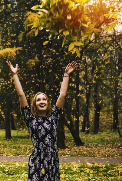 Caucasian woman tossing autumn leaves in park
