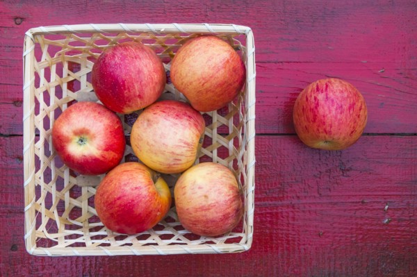 Close up of basket of red apples on red wooden table