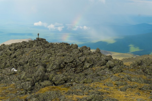 Man standing on rock formation looking at rainbow