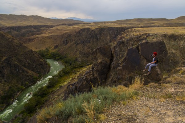 Caucasian woman sitting on mountain rocks photographing river