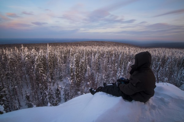 Caucasian man sitting in snow admiring scenic view of forest