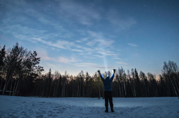 Caucasian man wearing headlamp with arms raised in winter