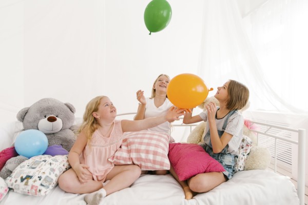 Middle Eastern sisters sitting on bed playing with balloons