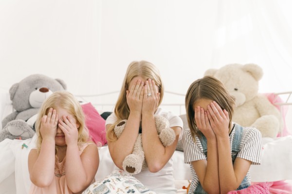 Middle Eastern sisters sitting on floor in bedroom covering eyes